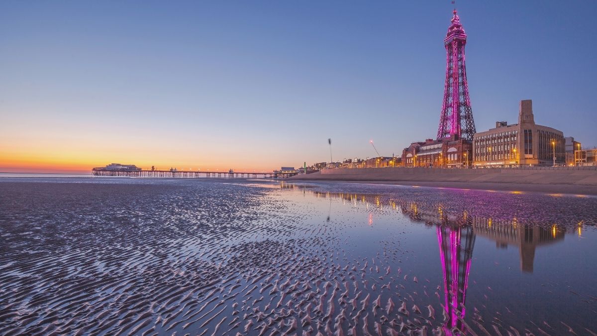 Blackpool Tower lit pink at dusk, reflected on the beach along the seafront
